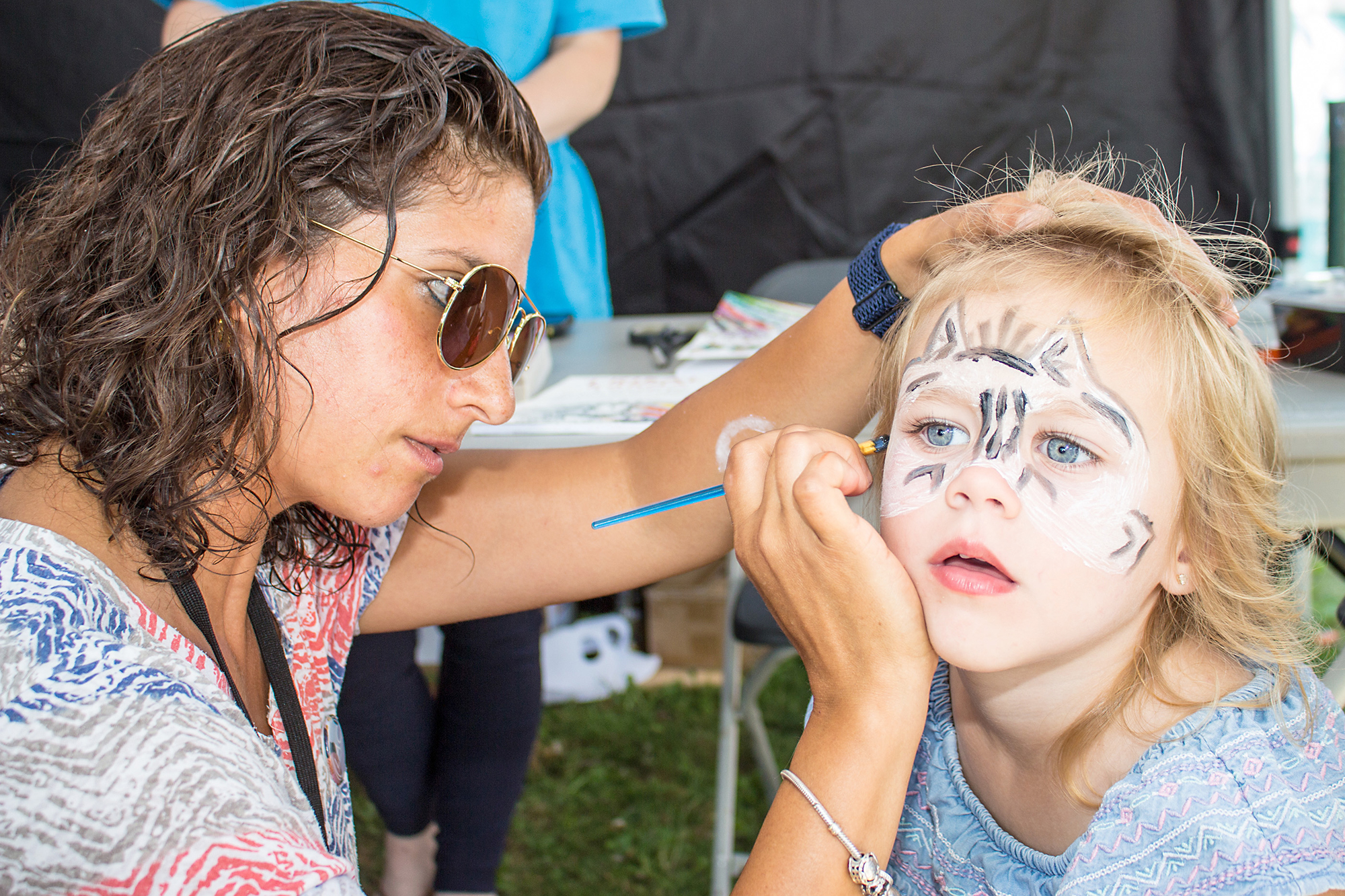 Three-year-old Stella gets her face painted by volunteer Maissaa.