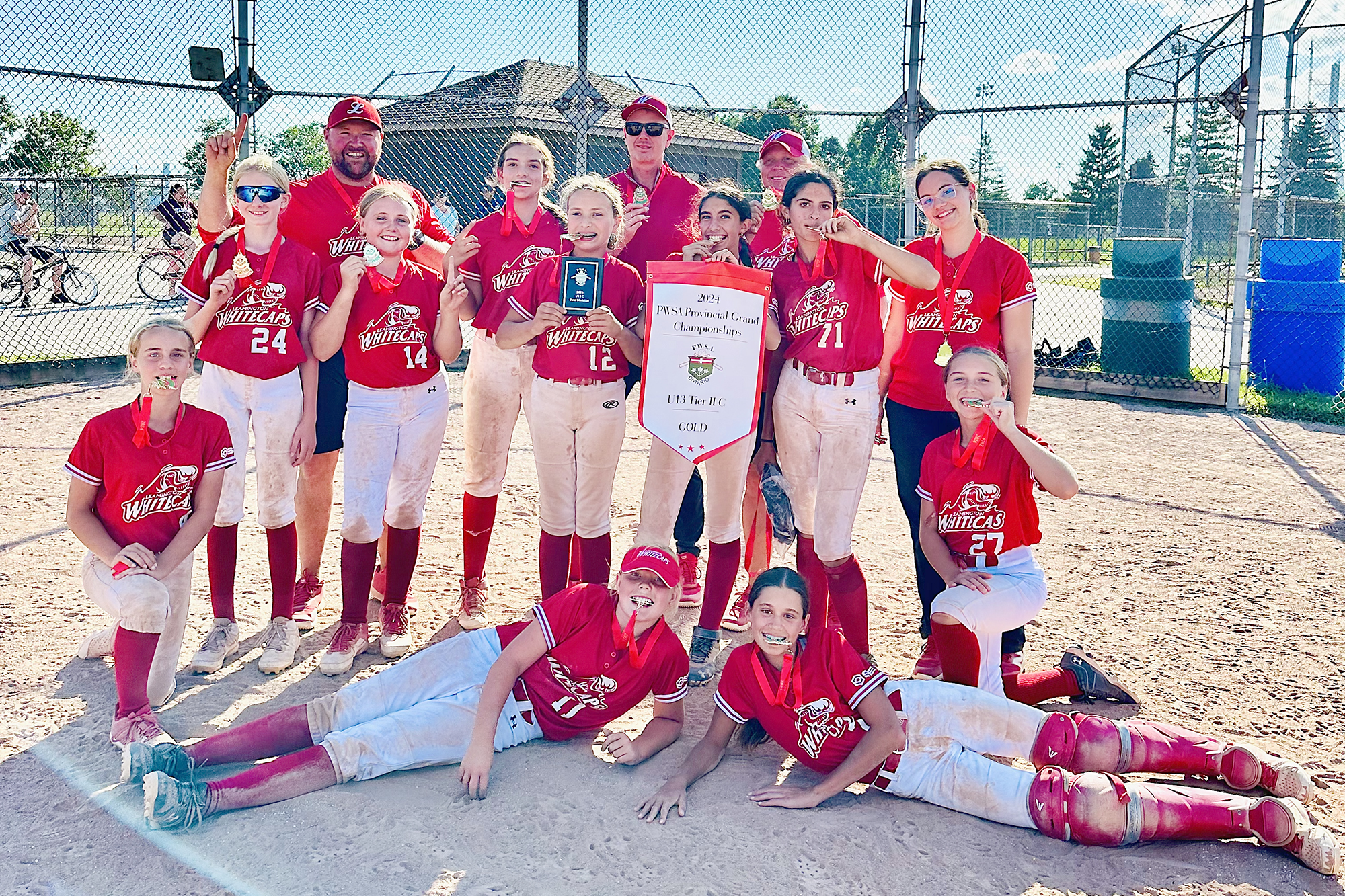 Team photo of the U13 Whitecaps team in front of home plate with the championship banner.