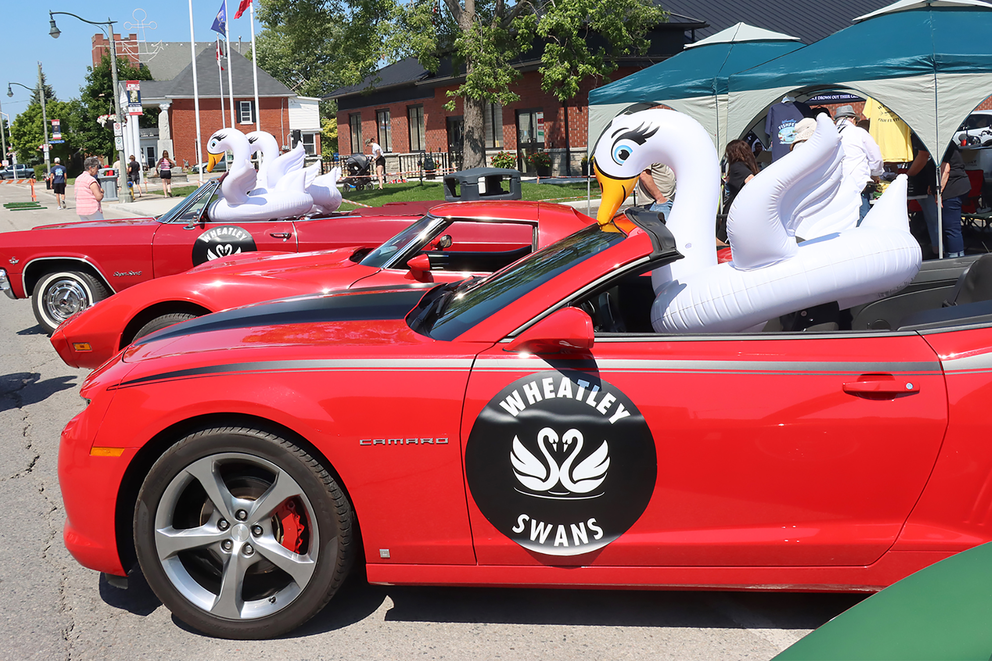 Two decorated Wheatley Swans vehicles drive through the Fish Festival Car Show in Wheatley.