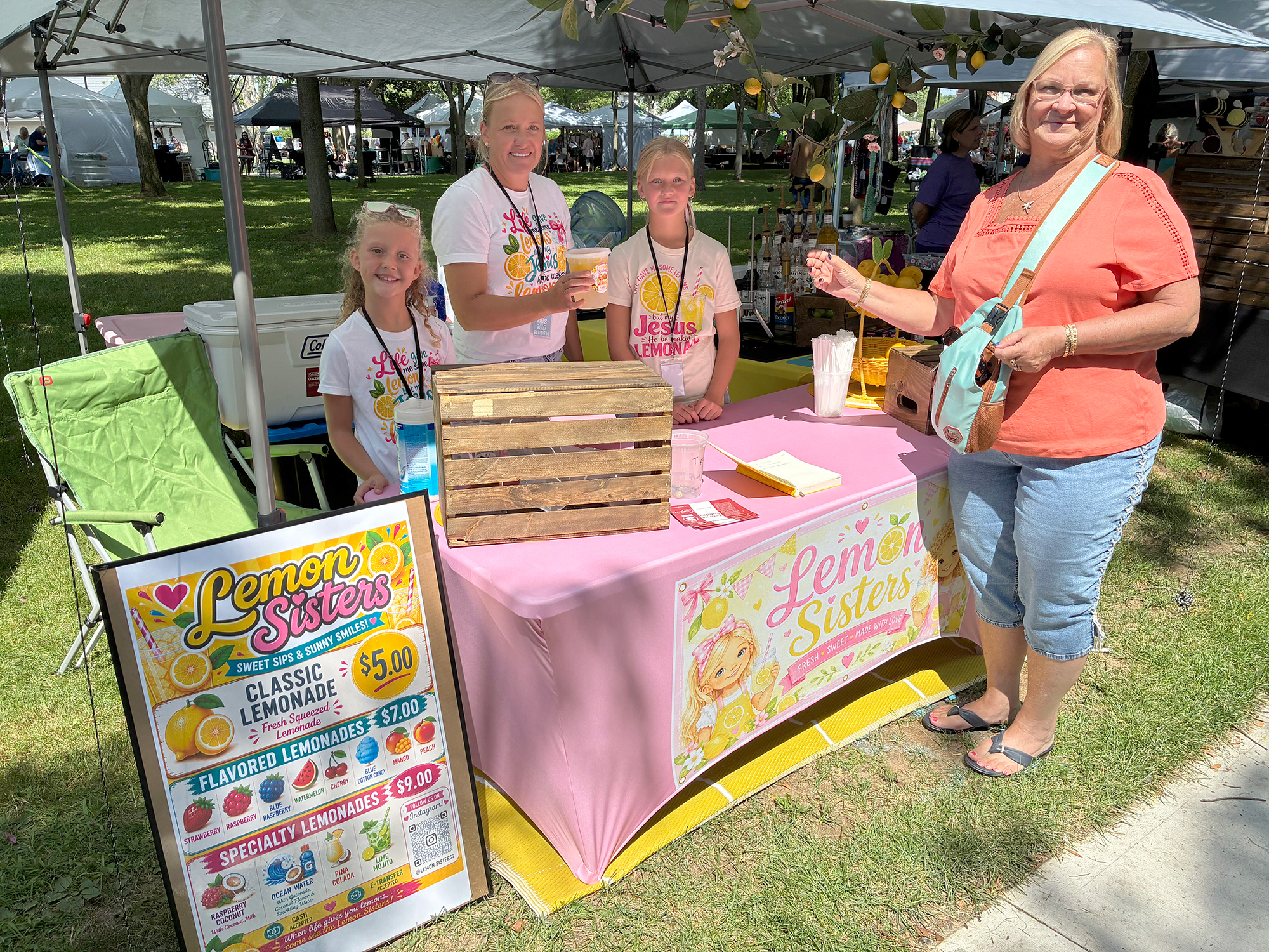 Mary Wall and daughters Laila and Ariana of Lemon Sisters serve a mango lemonade to Ruth Garant at Arts at the Marina 2026.
