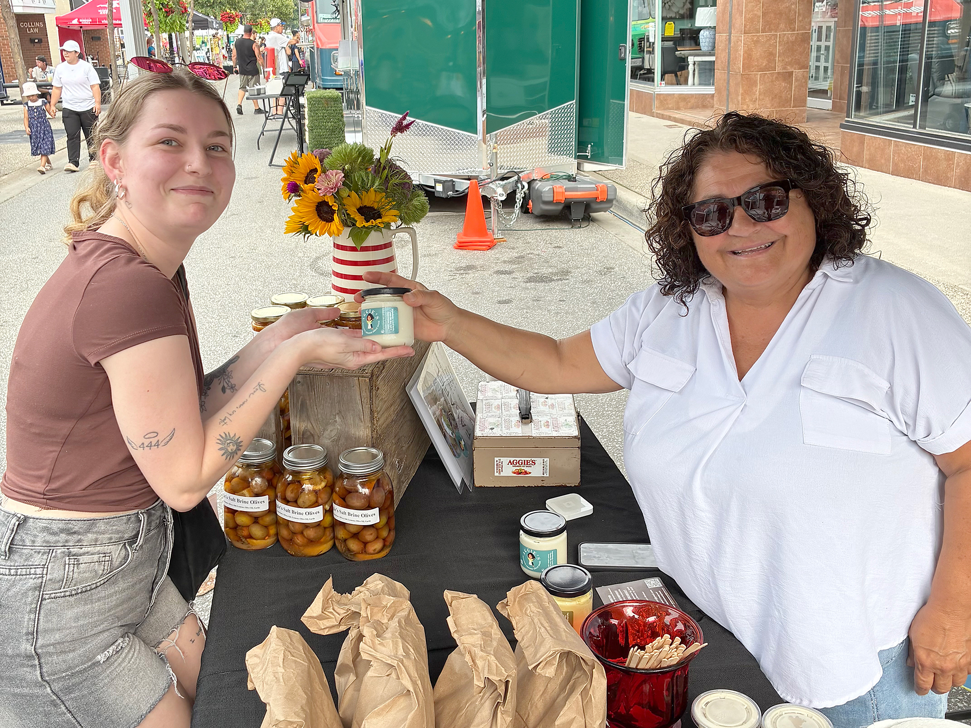 Jayden Grenier purchases a jar of garlic sauce from Aggie Toole of Aggie’s Authentic Garlic Sauce at the Mill Street Market.