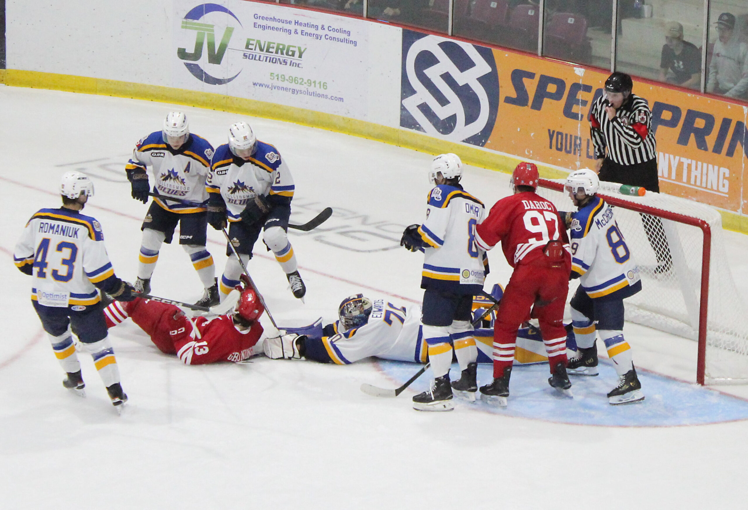 Flyers’ forward Griffin Grundner (13) is knocked to the ice by a pair of Collingwood players as Blues’ goalie Owen Edwards reaches to snare a rebound while Flyer Ashton Darocy (97) is covered to the right side of the net.