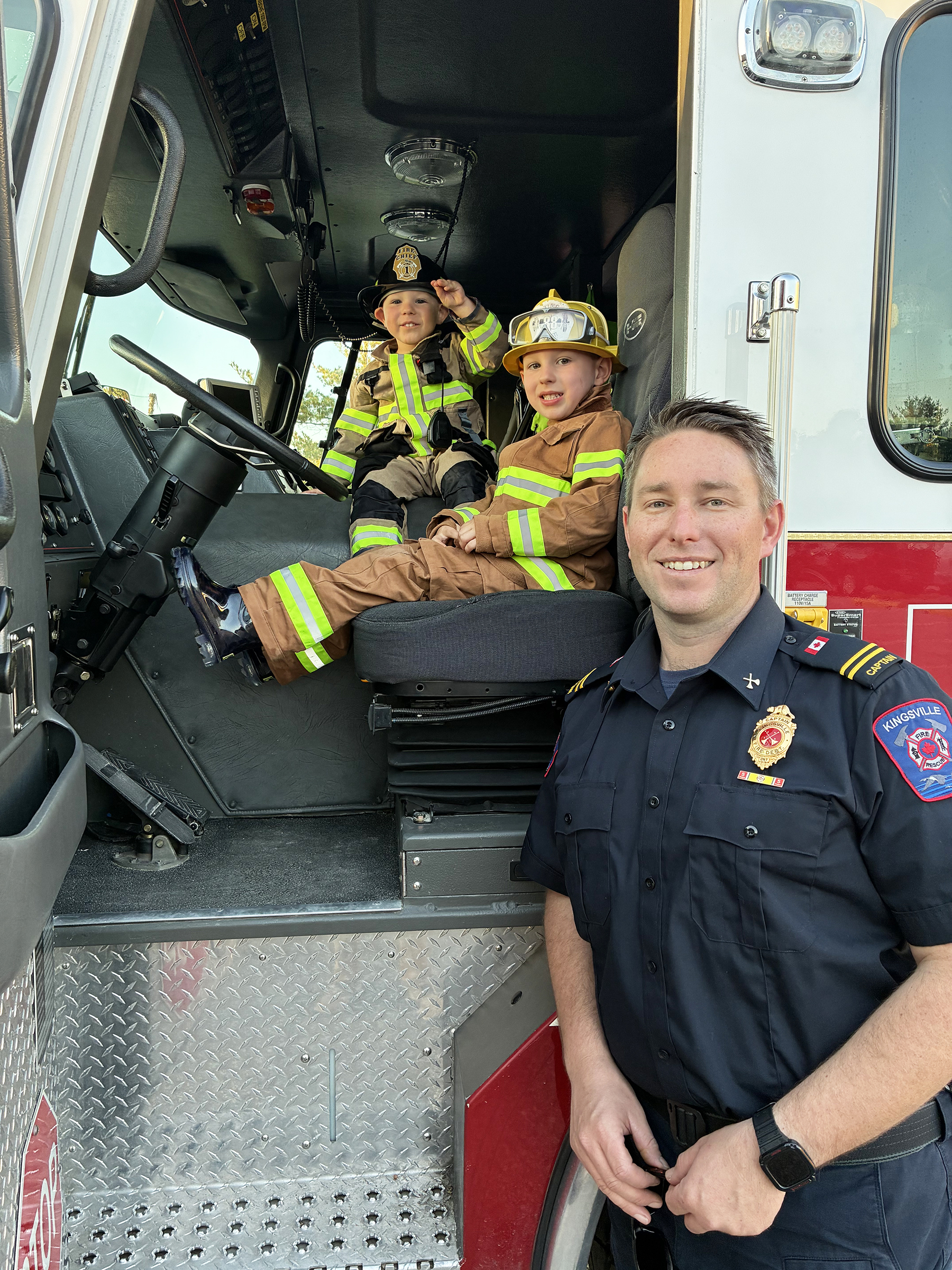 All decked out in their fire gear at the wheel of the 95-foot aerial truck are brothers Loic and Leo, along with Kingsville Fire Department Captain Matt Stewart.